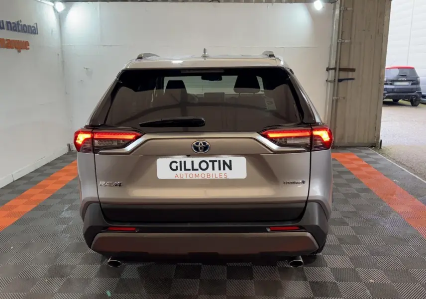 Vue arrière d'un Toyota RAV4 hybride gris clair avec feux LED allumés dans un garage.
