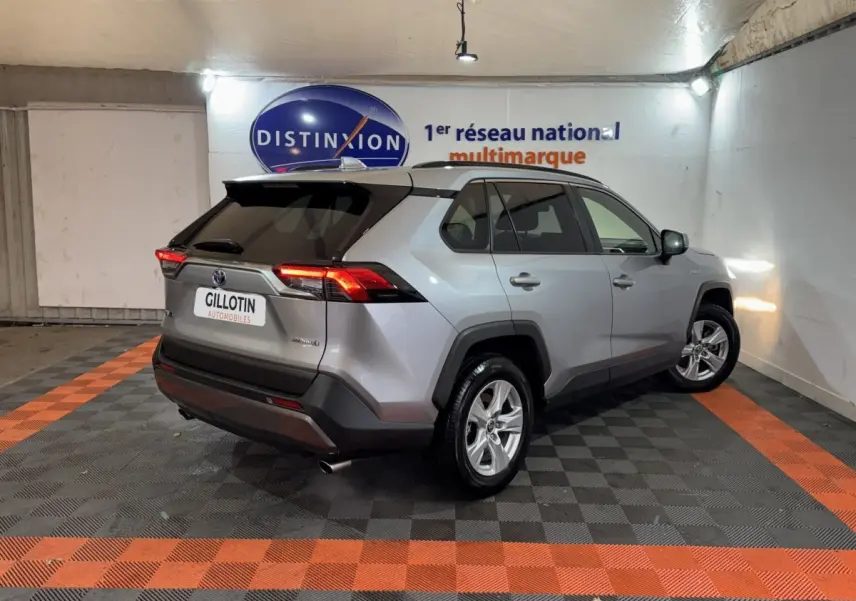 Toyota RAV4 hybride gris clair vu en 3/4 arrière droit dans un showroom avec éclairage intérieur.