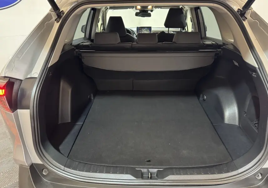 Coffre ouvert vu de l'arrière d'un Toyota RAV4 gris clair, montrant un espace de chargement spacieux avec cache-bagages.