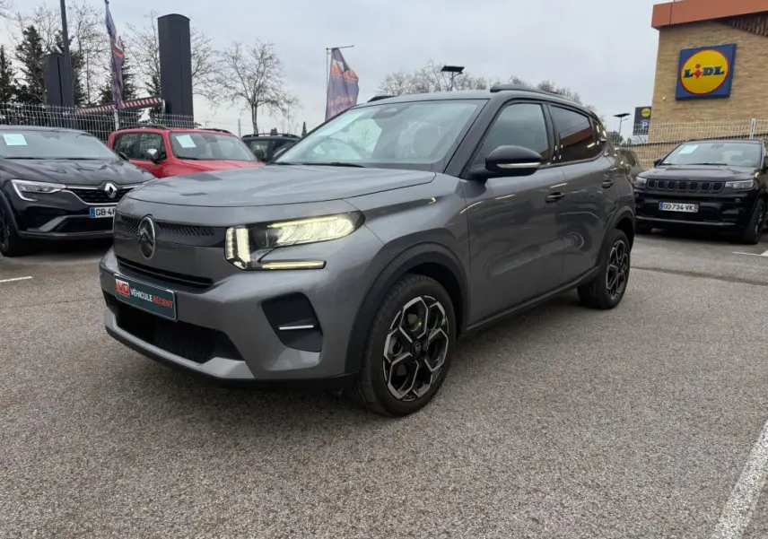 Citroën C3 gris vue 3/4 avant droit, avec jantes alliage noires et barres de toit visibles en extérieur.
