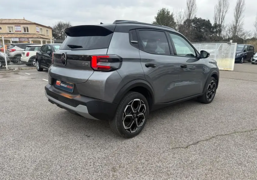 Vue 3/4 arrière droite d'une Citroën C3 gris métallisé avec jantes alliage noires et barres de toit visibles.