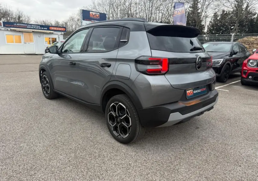 Vue 3/4 arrière droite d'une Citroën C3 gris métallisé avec jantes alliage 17 pouces et barres de toit noires.