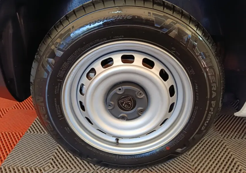Gros plan sur la roue acier grise avec logo Peugeot, montée sur un Peugeot Partner blanc, vue latérale.