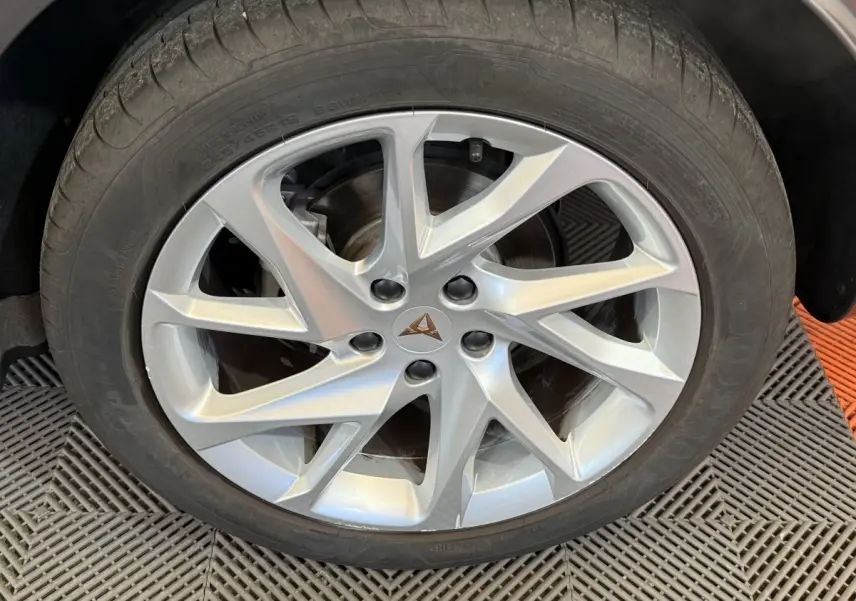 Gros plan sur la jante argentée au design dynamique avec logo CUPRA, roue montée sur un véhicule noir.