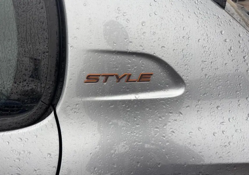 Gros plan sur l’inscription Style en relief sur la porte arrière droite d’une Peugeot 208 gris métallisé sous la pluie.