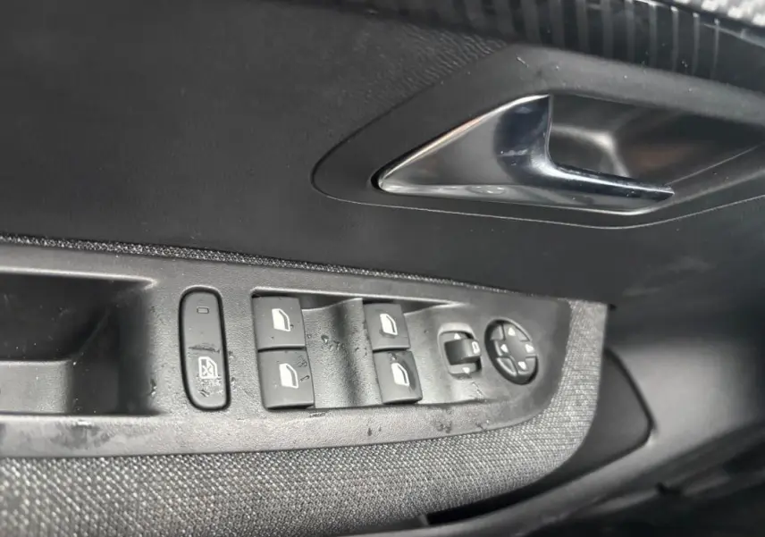 Gros plan sur la commande des vitres électriques côté conducteur d’une Peugeot 208 Hybrid gris, avec poignée de porte chromée.