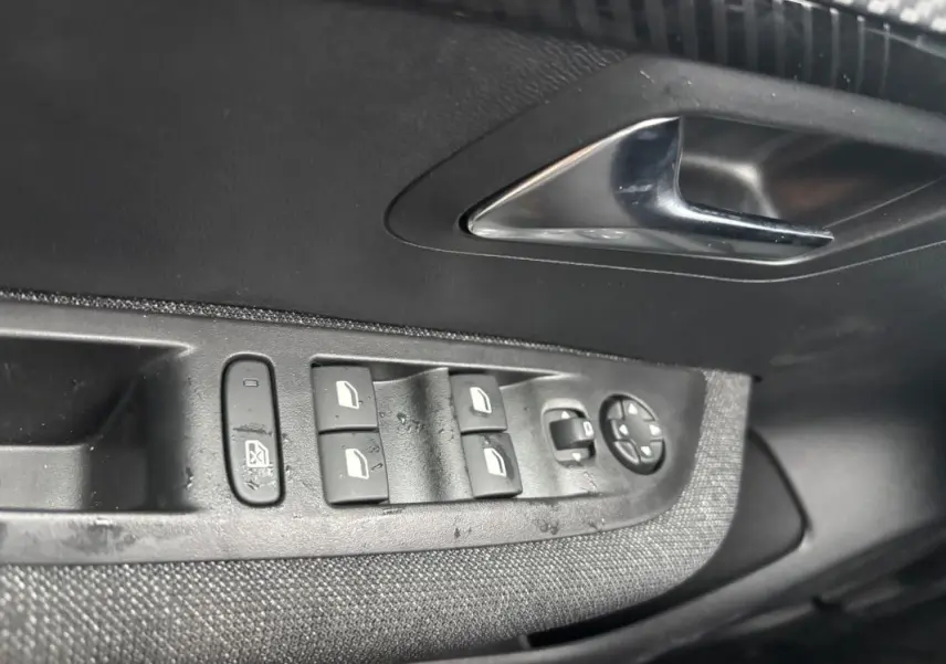Gros plan sur les commandes des vitres électriques et rétroviseurs sur la porte intérieure côté conducteur d'une Peugeot 208 gris hybride.
