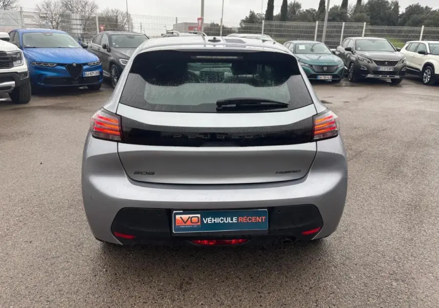 Vue arrière d’une Peugeot 208 Hybrid gris 2025 avec feux LED allumés et logo distinctif sur un parking.