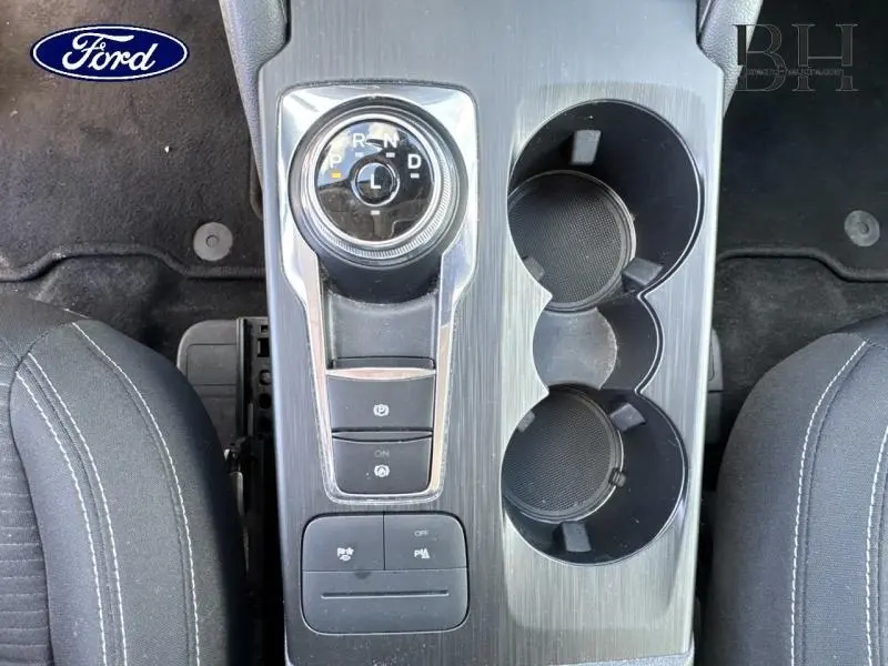 Vue plongeante sur la console centrale grise du Ford Kuga 2023, avec sélecteur rotatif de boîte auto et porte-gobelets.