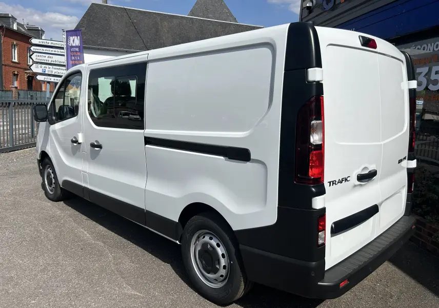 Renault Trafic cabine approfondie blanc en 3/4 arrière droit, portes latérales coulissantes et vitres passagers visibles.