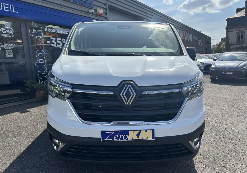 Vue avant d’un Renault Trafic cabine approfondie blanc, avec calandre noire et logo Renault bien visible, stationné en extérieur.