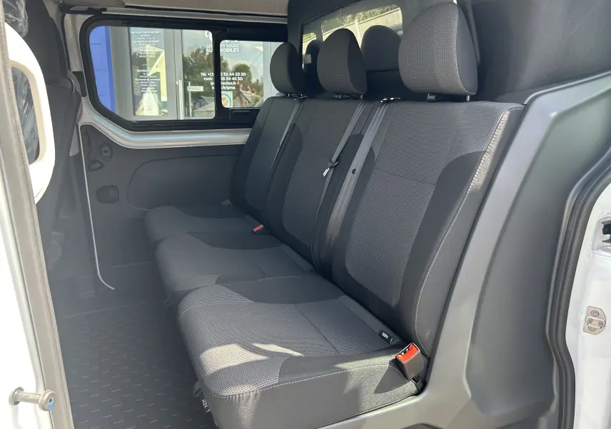 Vue latérale intérieure montrant la banquette arrière 3 places en tissu gris du Renault Trafic cabine approfondie blanc.
