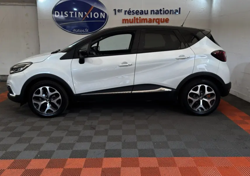 Vue de profil côté gauche d'un Renault Captur blanc avec toit noir, jantes alliage et protections noires sur les bas de caisse.