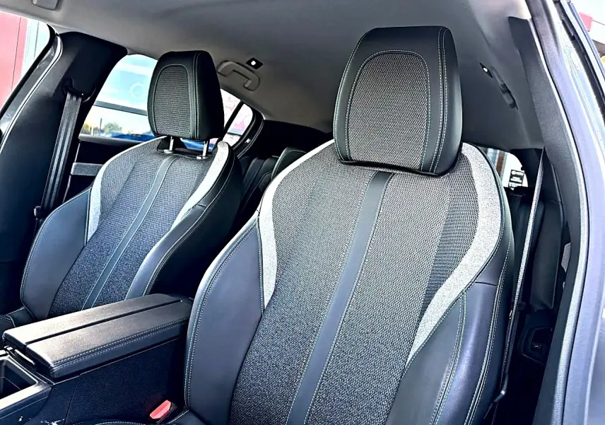 Vue intérieure rapprochée des sièges avant gris foncé avec surpiqûres claires et accoudoir central de la Peugeot 308 2025.