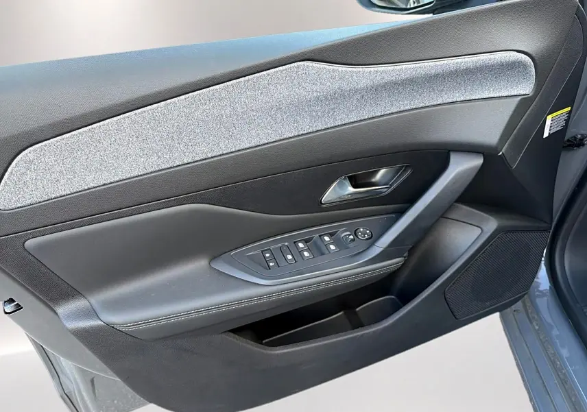 Vue rapprochée du panneau de porte avant gauche gris selenium de la Peugeot 308 1.5 BlueHDi 130 Allure EAT8 avec commandes de vitres et poignée chrome.