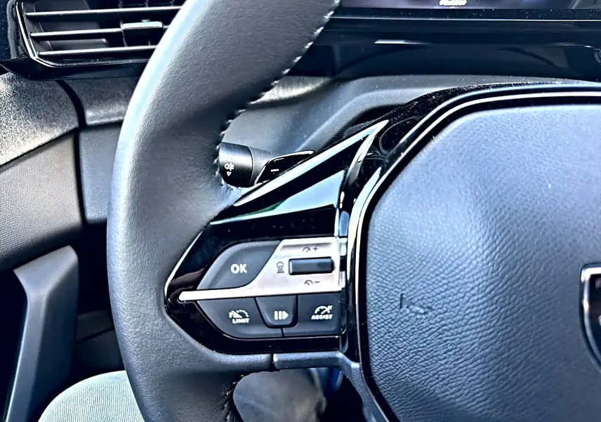 Gros plan sur le volant multifonction noir de la Peugeot 308 2025, avec commandes intégrées côté gauche.
