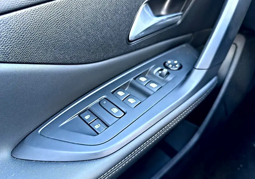 Gros plan sur la commande des vitres électriques et rétroviseurs sur la porte avant gauche en noir avec surpiqûres.