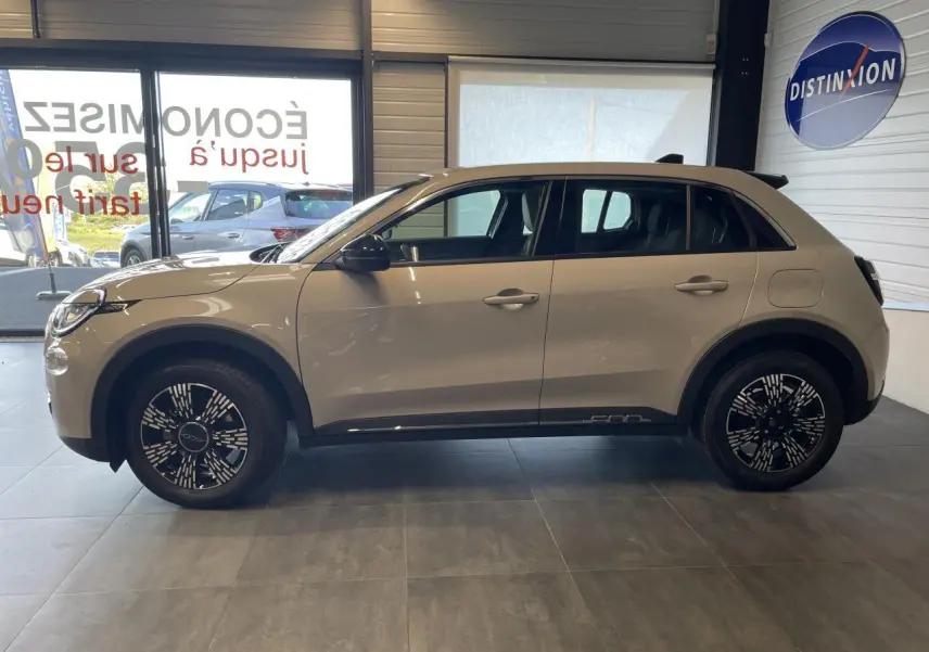 Profil côté gauche du FIAT 600 beige métallisé 2025 en intérieur, avec jantes alliage et rétroviseurs noirs brillants.