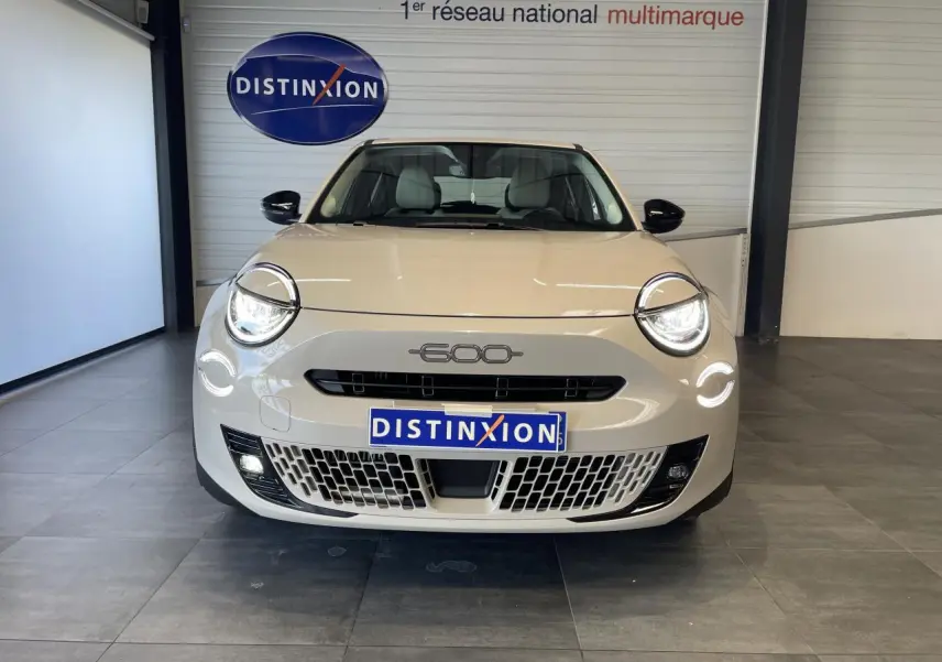 Vue frontale d'une FIAT 600 beige métallisé avec phares LED allumés et calandre ajourée, en showroom.