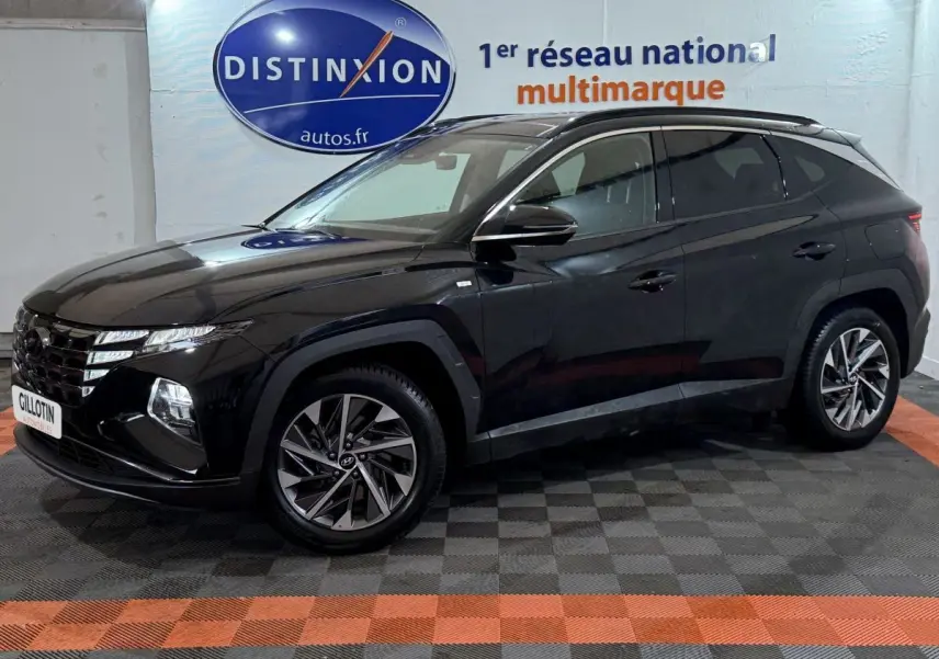 Vue 3/4 avant gauche d'un Hyundai Tucson noir brillant avec jantes alliage et vitres teintées en intérieur showroom.