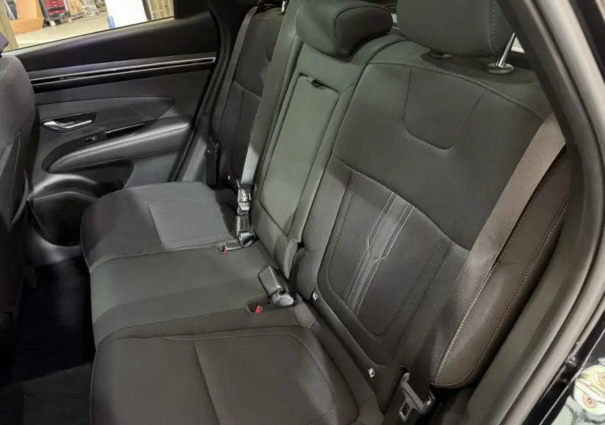 Vue intérieure du siège arrière côté gauche du Hyundai Tucson noir 2021, tissu sombre et ceintures visibles.