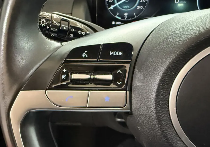 Gros plan sur les commandes du volant noir du Hyundai Tucson 2021, avec affichage digital du tableau de bord en arrière-plan.