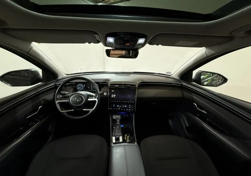 Vue intérieure avant du Hyundai Tucson noir 2021, avec tableau de bord numérique et toit ouvrant panoramique.