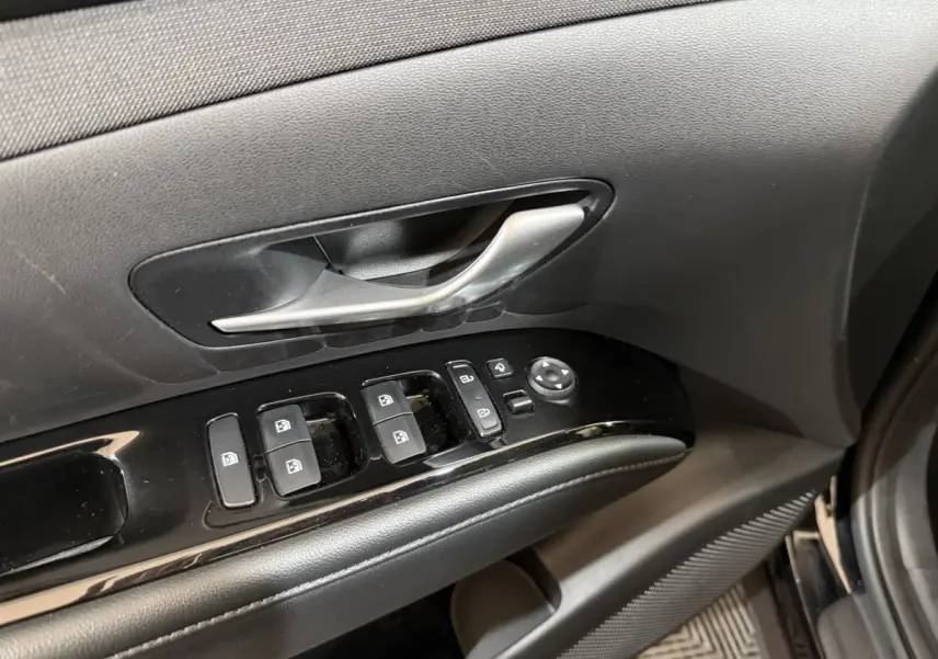 Gros plan sur la commande des vitres et la poignée intérieure côté gauche d'une Hyundai Tucson noir 2021.