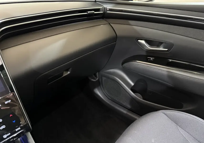 Intérieur noir du Hyundai Tucson 2021, vue côté passager avant sur tableau de bord et porte avec poignée métallique.