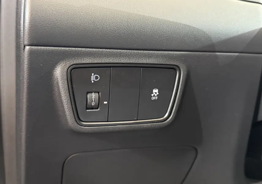 Gros plan sur les commandes de réglage des phares et de désactivation de l'antipatinage dans un Hyundai Tucson noir 2021.