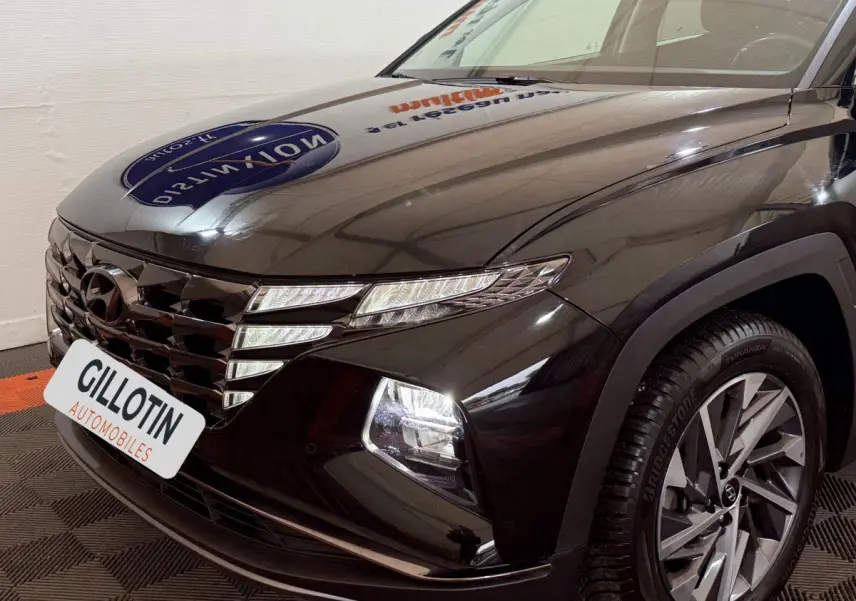 Vue 3/4 avant droit du Hyundai Tucson noir avec calandre distinctive et phares LED allumés.