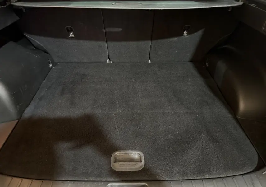 Vue intérieure du coffre noir du Hyundai Tucson 2021, version hybride 1.6 T-GDI, avec tapis de sol et sièges arrière rabattus.