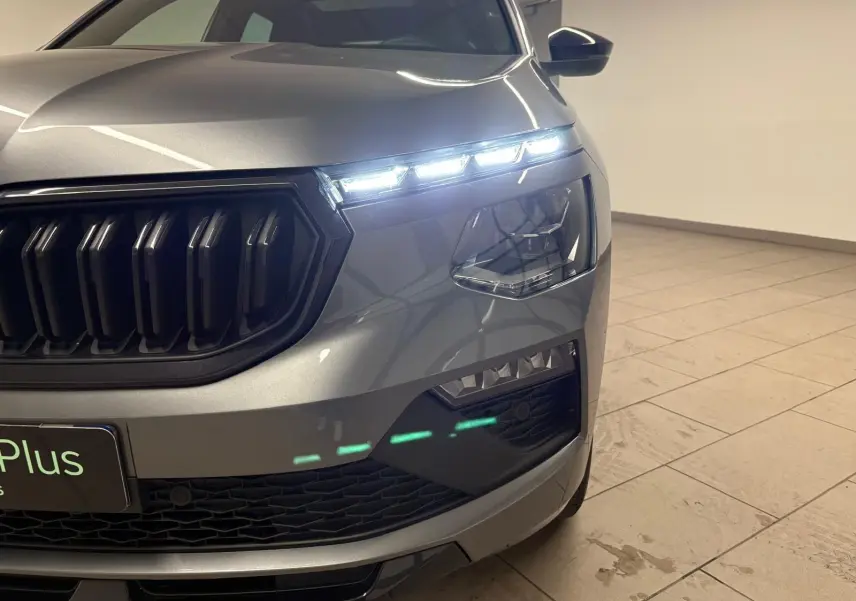 Gros plan sur l’avant droit du Skoda Kamiq Monte Carlo gris graphite 2024, mettant en valeur la calandre noire et les phares LED allumés.