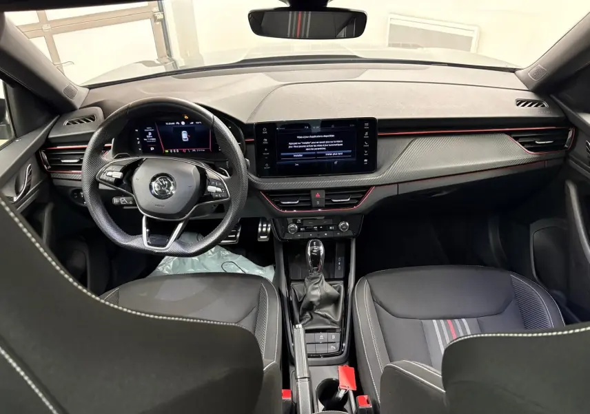 Vue intérieure avant du Skoda Kamiq Monte Carlo 2024, tableau de bord gris graphite avec touches rouges et volant multifonction.