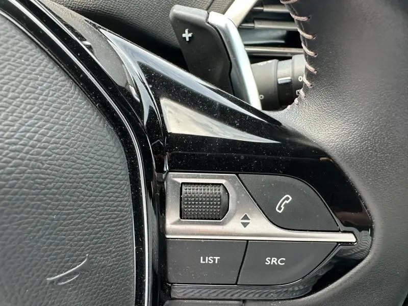 Gros plan sur les commandes multifonctions noires à gauche du volant cuir du Peugeot 3008 bleu hybride rechargeable 2024.