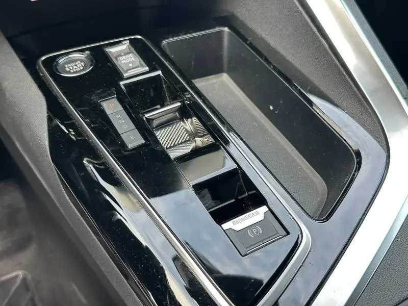 Gros plan sur la console centrale noire brillante du Peugeot 3008 Hybride Rechargeable 2024 avec levier de vitesses et bouton start/stop.