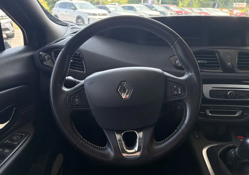 Vue centrée sur le volant en cuir noir du Renault Scenic gris Cassiopée, avec tableau de bord et commandes visibles.