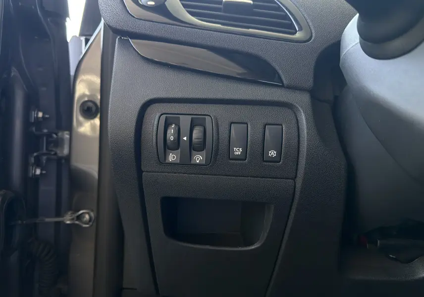 Vue intérieure côté gauche du tableau de bord d'un Renault Scenic gris cassiopée 2015, montrant les commandes de réglage des phares, TCS et arrêt auto.