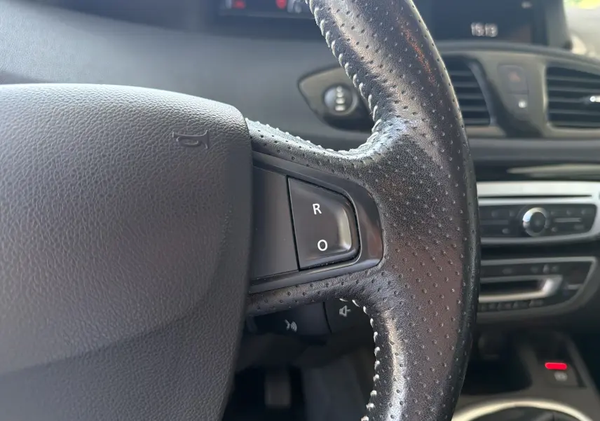 Gros plan sur le volant en cuir perforé côté droit du Renault Scénic gris, avec boutons de commande intégrés.