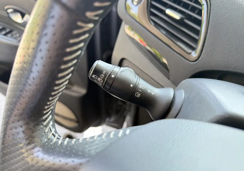 Gros plan sur la commande des feux et clignotants à gauche du volant perforé dans l’habitacle gris du Renault Scenic 2015.