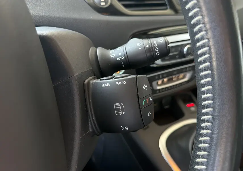 Gros plan sur la commande multimédia et le commodo d’essuie-glace à gauche du volant en cuir noir du Renault Scénic gris Cassiopée.