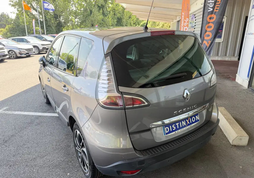 Vue 3/4 arrière droite d'un Renault Scénic gris Cassiopée 2015 avec jantes bi-ton et vitres teintées, stationné sous abri.
