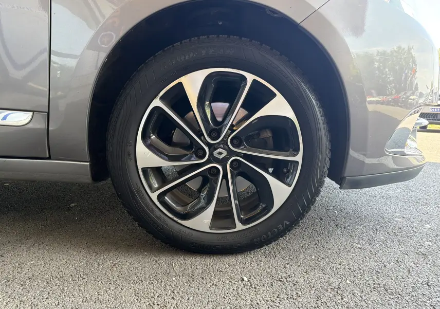 Gros plan sur la roue avant droite d’un Renault Scénic gris Cassiopée, jante alliage bi-ton avec logo Renault central.