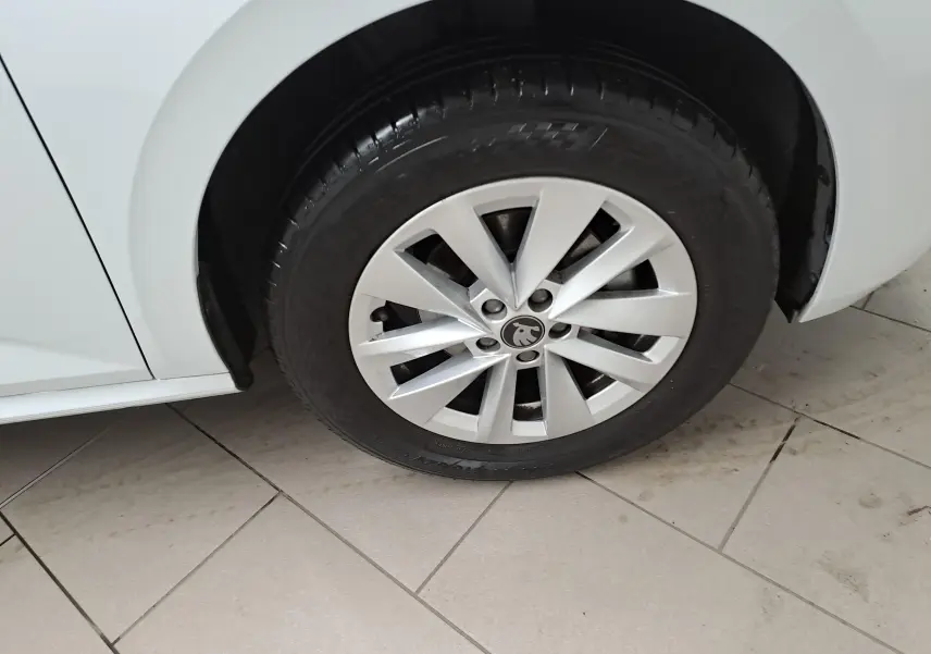 Gros plan sur la roue avant gauche d’un Skoda Kamiq blanc Lune, mettant en valeur la jante alliage et le logo central.