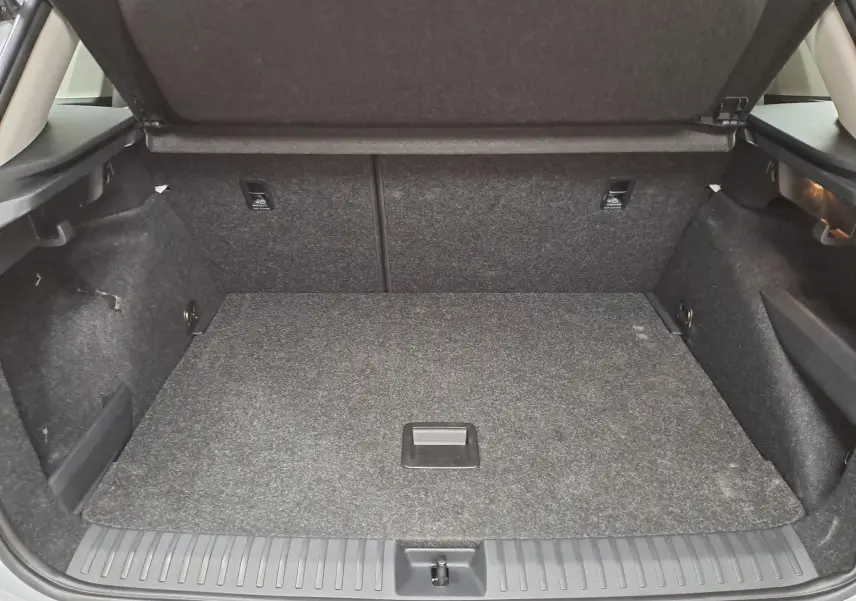 Coffre ouvert vu de l'arrière d'un Skoda Kamiq blanc Lune, montrant l'espace de chargement vide et la moquette grise.