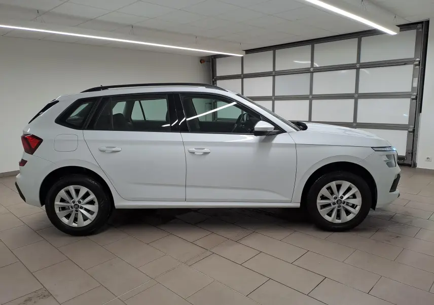 Vue de profil côté gauche d'un Skoda Kamiq blanc Lune 2025 dans un garage, soulignant ses lignes modernes et ses jantes alliage.