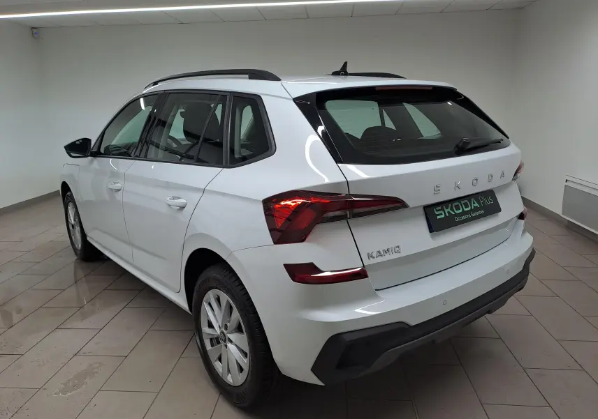 Vue 3/4 arrière droite d’un Skoda Kamiq blanc Lune avec feux arrière allumés et radars de stationnement visibles.