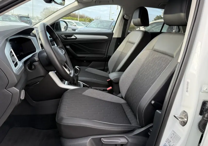 Intérieur côté conducteur du Volkswagen T-Roc blanc 2025, sièges tissu et cuir, volant multifonction et boîte manuelle visible.