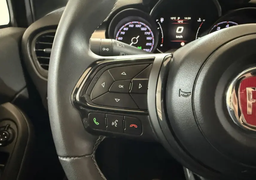 Gros plan sur le volant multifonctions noir de la Fiat 500X 2021 avec tableau de bord numérique en arrière-plan.