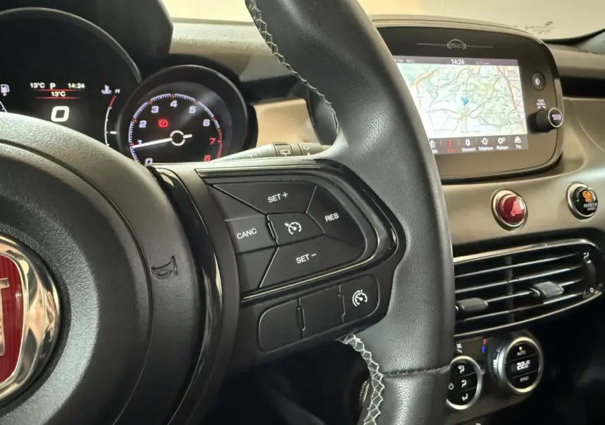 Vue rapprochée du volant cuir noir et du tableau de bord avec écran tactile et commandes du Fiat 500X noir 2021.